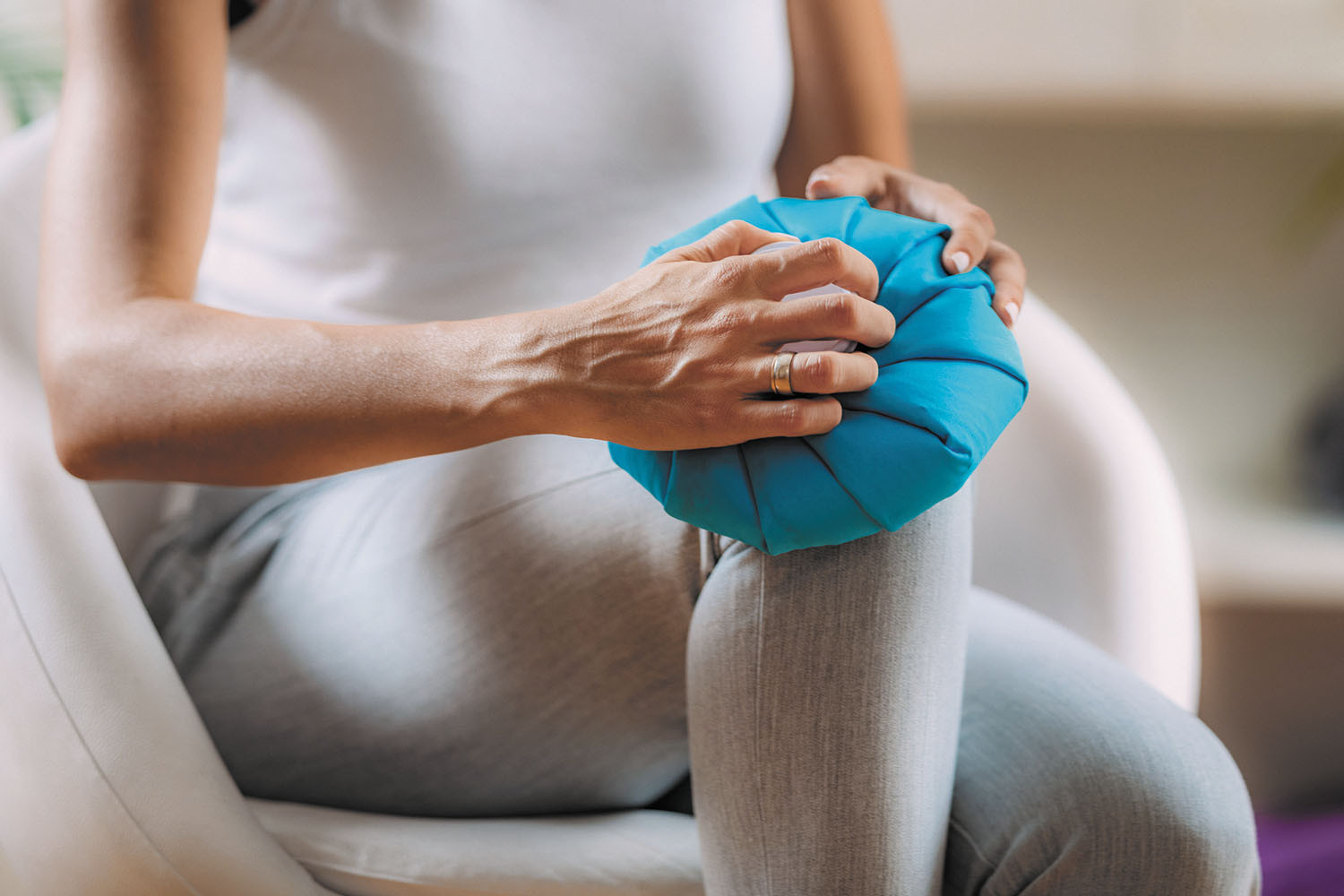 cropped photo showing from the neck down a woman holding an ice pack on her knee