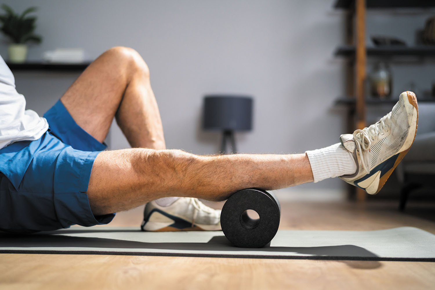 photo of a man sitting on a mat on the floor using a foam roller under his calf